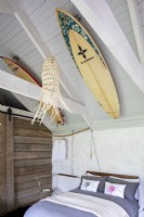 La maison de Sally et John Biddle à Cornwall, une chambre dans une grange aménagée. Poutres en bois et décoration rustique, planches de surf fixées au plafond