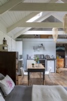 Grange convertie, avec vue sur cuisine simple et table de ferme en bois. Poutres en bois et décoration rustique.
