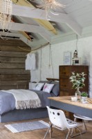 Grange aménagée, avec lit, meubles et bureau. Poutres en bois et décoration rustique, planches de surf décorant le toit en bois et une simple table en bois