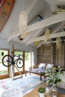 Grange aménagée, avec lit, meubles et support vélo. Poutres en bois et décoration rustique, planches de surf décorant le toit en bois