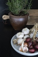 Bol de bulbes d'ail et d'oignons rouges à côté du pot de romarin - détail 