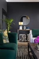 Canapé en velours vert, tapis graphique et murs noirs dans le salon 