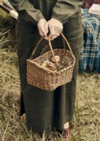 Femme en robe de lin vintage tenant un panier d'articles fourragers 